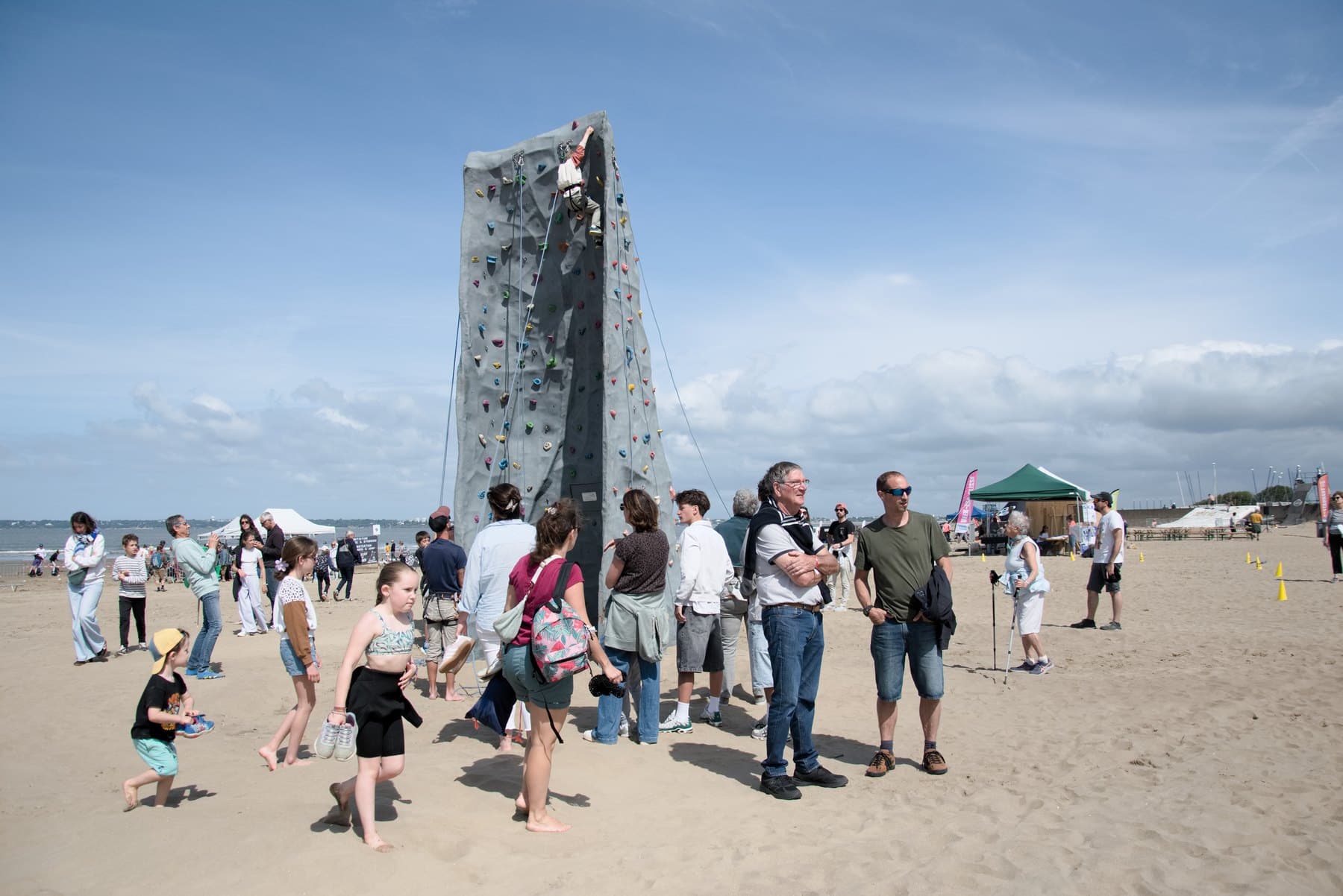 Le mur d'escalade installé sur une plage, entouré de visiteurs, lors d'un événement public